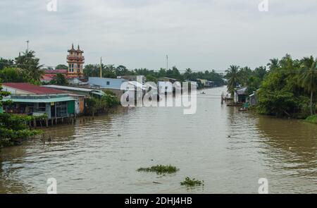 Mekong Delta in Vietnam. Boats in river with brown water. Houses of local citizens on the bank of river. Stock Photo