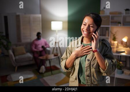 African young woman smiling while talking on mobile phone standing at office with man in the background Stock Photo