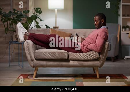 African young man resting on sofa with mobile phone during his leisure time Stock Photo