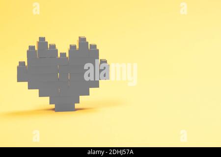 Gray heart made of plastic constructor blocks on yellow background. Stock Photo
