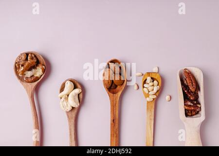Wooden spoons with pecans, walnuts, almonds, pine nuts and cashews on pink backround, top view Stock Photo