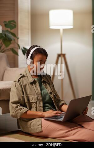 African woman in headphones working online on her laptop sitting on sofa at home Stock Photo