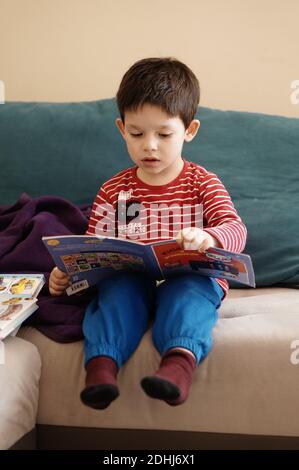 POZNAN, POLAND - Nov 15, 2017: Young three years old boy reading a book by a sofa. Stock Photo