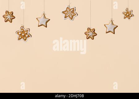 Christmas baking concept with gingerbread cookies. Christmas snowlakes and stars cookies hanging on threads over pastel beige, champagne background. Copy space for text Stock Photo