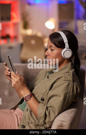 Young woman wearing headphones using digital tablet for online reading on the sofa at home Stock Photo