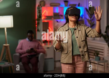 Young woman wearing VR glasses standing and gesturing playing in virtual reality game Stock Photo