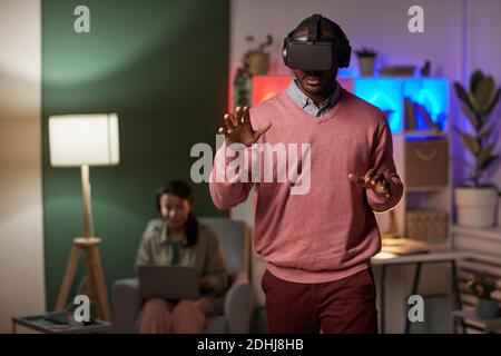 African man wearing glasses standing in the room and gesturing while playing in virtual reality game Stock Photo