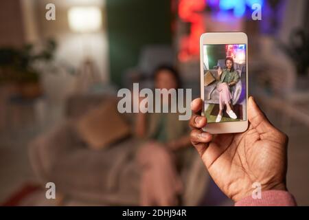 Man holding mobile phone photographing young woman who posing on the sofa Stock Photo