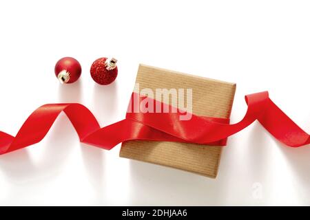 Christmas presents homemade packaging. Holiday preparation. Making bow with a shiny red ribbon, wrapping decoration of a brown paper gift box, isolate Stock Photo