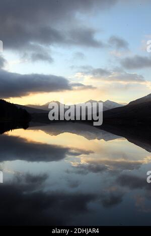 Sunset over the Snowdon horseshoe across showing recent snowfall beyond a flat calm Llynnau Mymbyr. Wales. Picture taken 5th December 2020