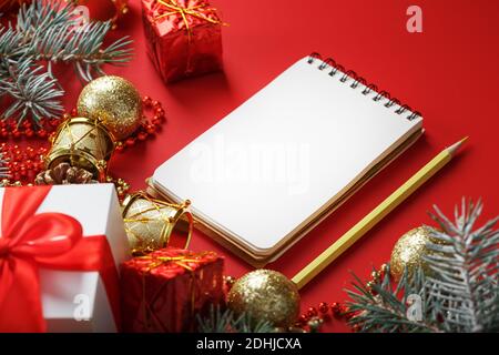 Christmas composition with notepad and a pencil for writing wishes with Christmas tree decorations on a red background. Christmas mood and plans for t Stock Photo