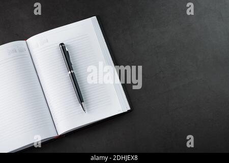 Black Notepad with a black pen on a black background. Top view, minimalistic concept. Free space. Stock Photo