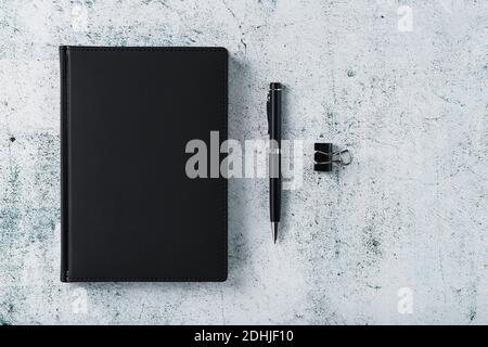 Office desk with black notepad and pen on gray background. Top view with copy space. Business goals and objectives concept Stock Photo