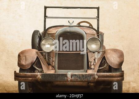 Retro styled image of an over a century old rusted and broken classic car in front of an old wall Stock Photo