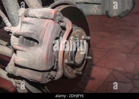 Rusty front hub of a car wheel with a brake disc and a red caliper. A car without a wheel. Close up Stock Photo