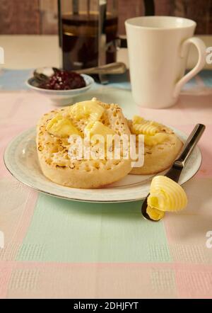 Traditional hot buttered toasted crumpets on a white plate on a table setting, with melted butter ready to eat. Stock Photo