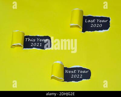 Text written on yellow torn paper with dark background. - Last year 2020, this year 2021 and next year 2012