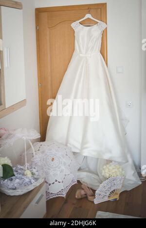 A vertical shot of a beautiful white wedding dress hanging by the door in the bride's room Stock Photo