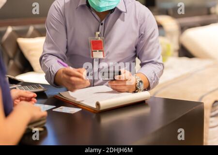 Seller in protective mask hand holding credit card and writing card detail. Stock Photo
