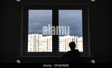 A lonely child looks out the window of his house in an apartment. Stock Photo