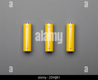 Three yellow AA alkaline batteries or rechargeable cells on gray background trendy colors of the year 2021 toned concept Stock Photo
