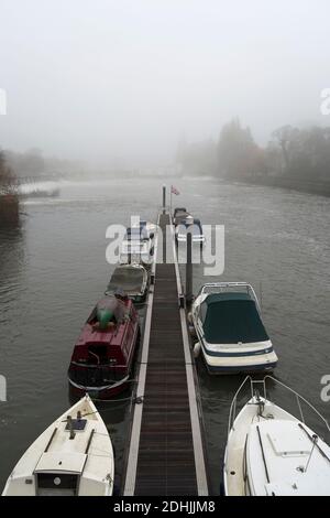boats moored on a jetty at teddington lock, southwest london, england, on a foggy morning in winter with teddington weir in distance Stock Photo