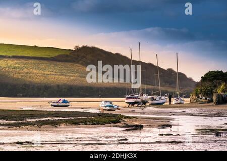 Evening light over boats moored and beached on the foreshore of the Gannel River at low tide in Newquay in Cornwall. Stock Photo
