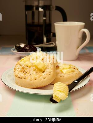 Traditional hot buttered toasted crumpets on a white plate on a table setting, with melted butter ready to eat. Stock Photo
