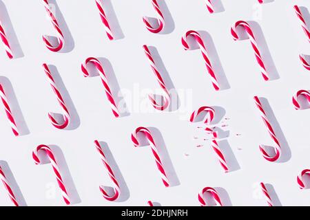 Top view full frame composition of red and white striped Xmas candy canes arranged in rows with one cane broken on white background Stock Photo