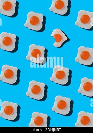Top view of pattern of whole sweet candies in shape of fried eggs with one bitten arranged on blue background Stock Photo