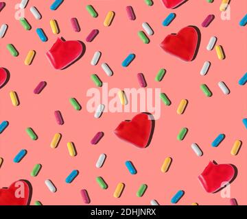 Top view of pattern of red heart shaped and colorful small jelly candies on pink background Stock Photo