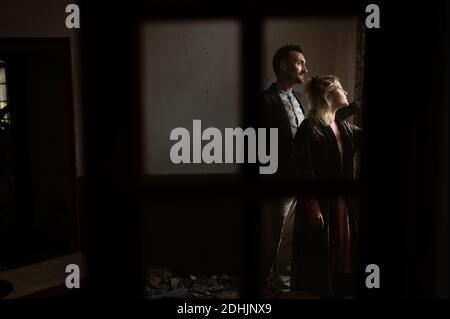 Side view of calm peaceful man and Woman in old fashioned outfits standing near window in dark room and looking away dreamily Stock Photo