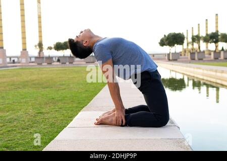 Side view of Asian male in sportswear standing in Ustrasana in backbend and practicing mindfulness while doing yoga and stretching body Stock Photo