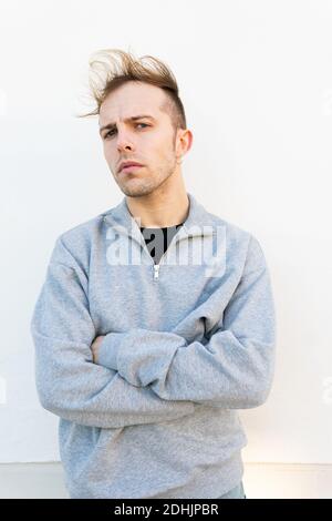 Modern unshaven hipster male in casual sweatshirt standing against wall on street looking at camera Stock Photo