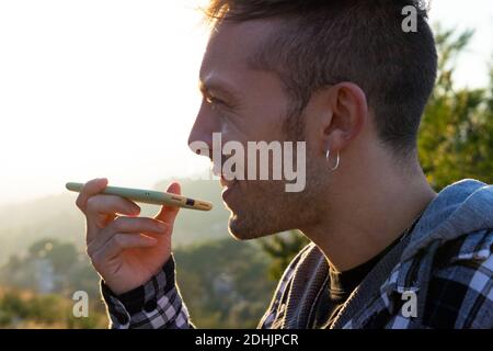 Young cheerful tourist in face mask and eyeglasses standing near river behind mountains while looking away Stock Photo
