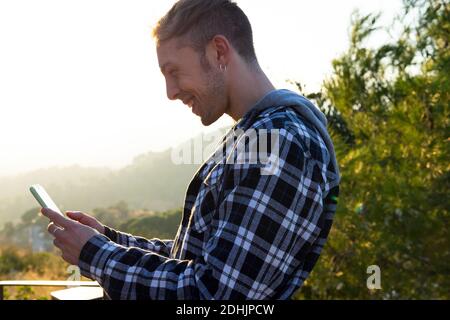 Side view of delighted young hipster male in casual outfit getting great news on mobile phone while resting in countryside Stock Photo
