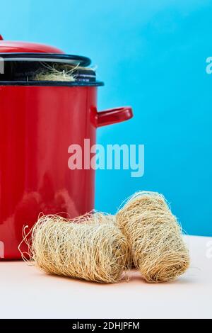Natural eco friendly loofah sponges for washing dishes placed on table near saucepan in studio on vivid blue background Stock Photo