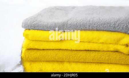 Stack of towels in Color of the Year 2021 - bright illuminating yellow and gray colours on white snow, isolated. Concept of Color of the Year 2021. Stock Photo
