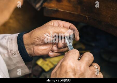 Closeup of crop unrecognizable mature male goldsmith using pliers while working with metal piece and creating jewelry in workshop Stock Photo