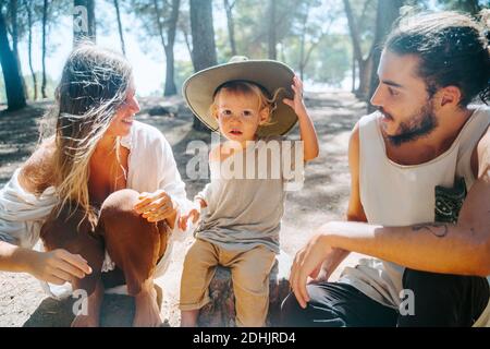 Multiethnic couple of hippie and cute little kid sitting barefoot in woods on sunny day and relaxing Stock Photo