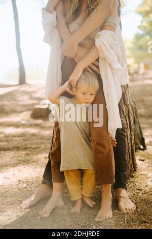From above of barefoot legs of crop parents standing with cute little baby on ground in forest on sunny day Stock Photo