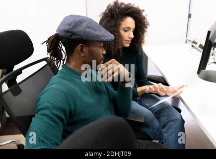 Positive young black African American Woman and male colleague in casual clothing sitting at table and analyzing business results while working togeth Stock Photo
