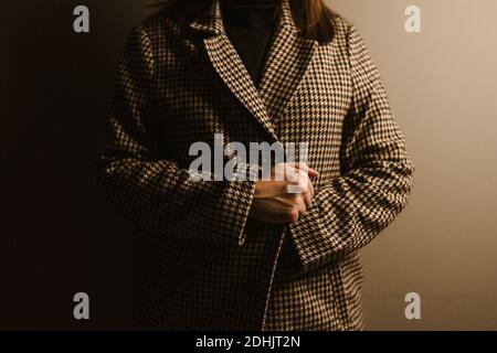 Cropped unrecognizable Woman in trendy checkered coat standing against brown wall Stock Photo