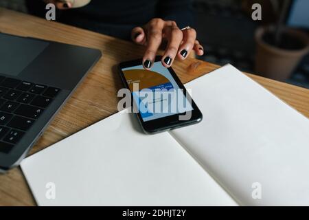 From above of crop anonymous female sitting at table with cup of coffee and analyzing diagram on smartphone while working on online project Stock Photo