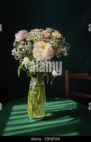 High angle of elegant bouquet of white gypsophila and pink peony flowers in glass vase placed on rustic table Stock Photo
