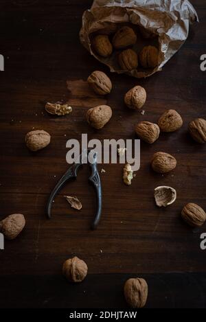 From above of pile of whole and cracked walnuts with kernels placed with nutcracker on dark wooden surface Stock Photo