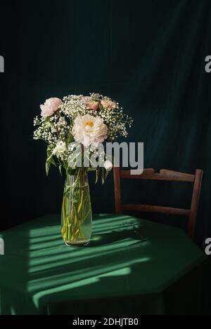 High angle of elegant bouquet of white gypsophila and pink peony flowers in glass vase placed on rustic table Stock Photo