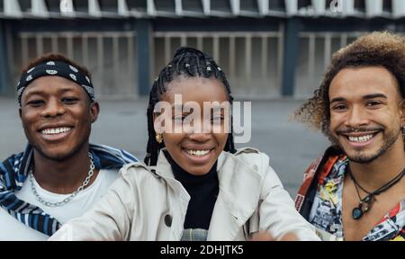 Group of cheerful young African American hipster friends in trendy outfits looking at camera and smiling happily while taking selfie together on urban Stock Photo