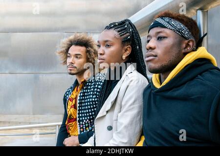 Serious unemotional young African American friends in casual informal clothes standing on stairway looking away while spending time together in city Stock Photo