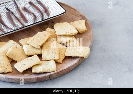 Heap of crispy salt crackers served on wooden board near plate with canned fish as appetizer Stock Photo